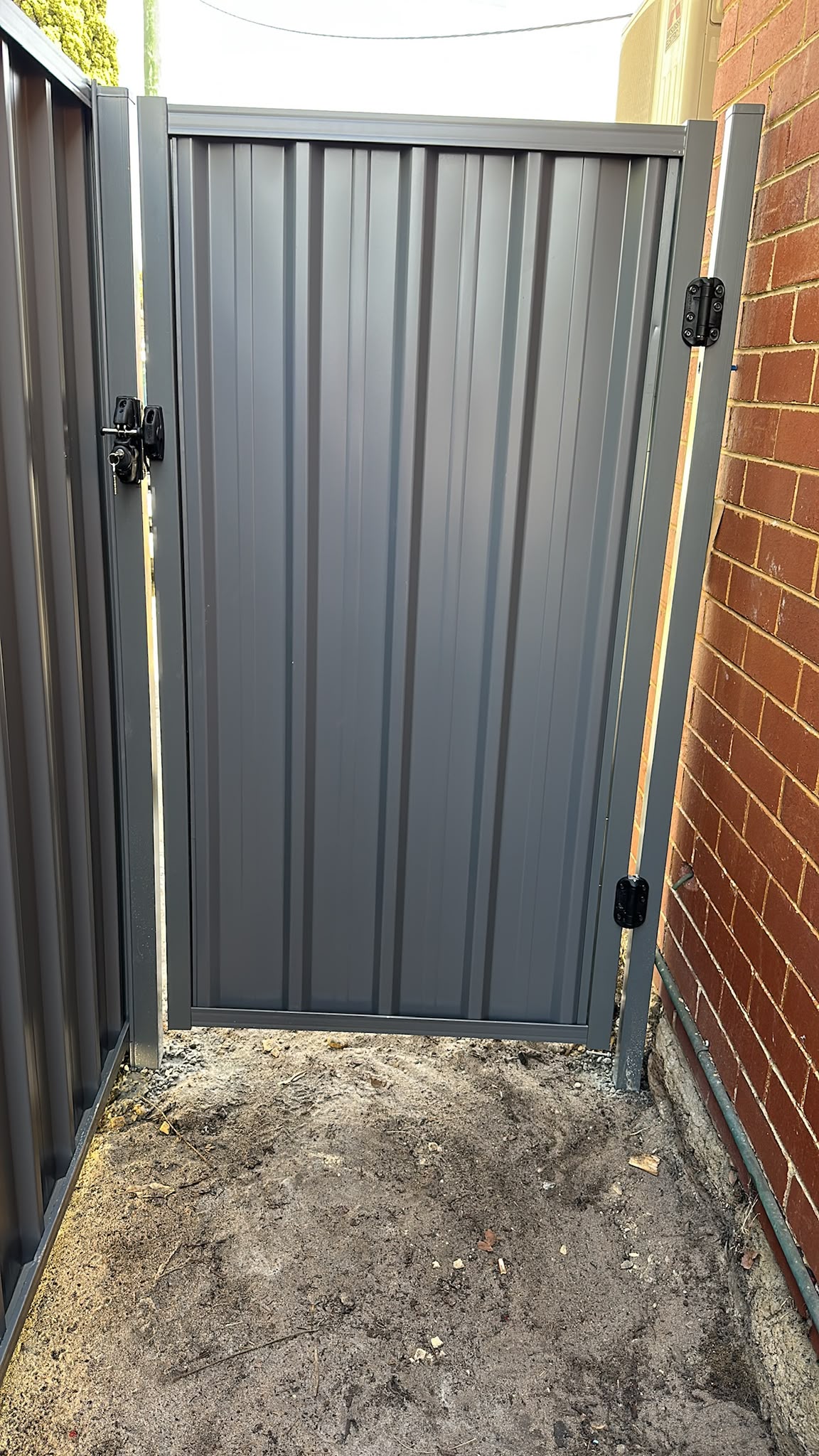 Grey Colorbond pedestrian gate installed beside a brick home